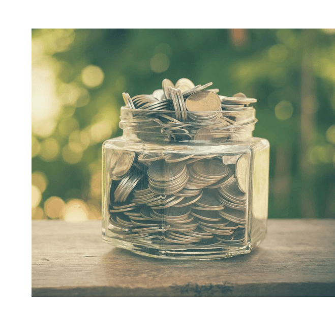 A glass jar filled with coins on top of a wooden table.